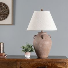 a table lamp sitting on top of a wooden dresser next to a potted plant