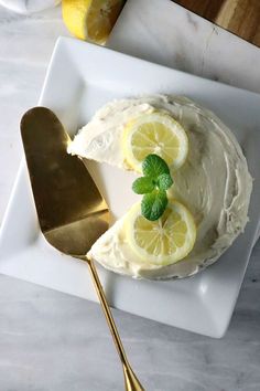 a white plate topped with a cake covered in frosting and lemon slices next to a gold spoon