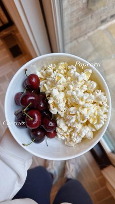 a person holding a white bowl filled with popcorn and cherries