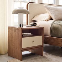 a nightstand with a lamp on top of it next to a bed