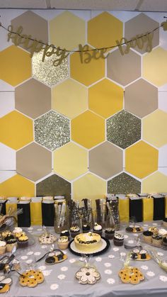 a table topped with cakes and cupcakes next to a yellow hexagonal wall