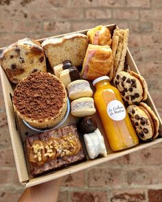 a person holding up a box filled with different types of breads and pastries