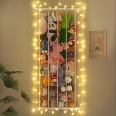 a bunch of stuffed animals in a cage with fairy lights on the wall behind them