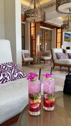 two glasses filled with drinks sitting on top of a table in a living room next to a couch