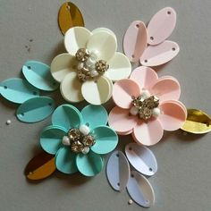 several different colored flower shaped hair clips on top of a gray surface with gold, white and pink accents