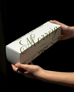 a person holding a white box with green writing on it and two hands reaching for it