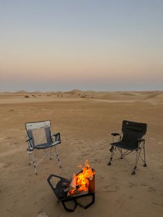 two chairs sitting in the sand near a campfire