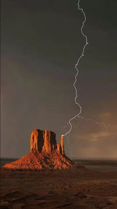 a lightning bolt strikes across the sky over a desert landscape with a rock formation in the foreground