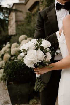 a bride and groom standing next to each other in front of some bushes with white flowers