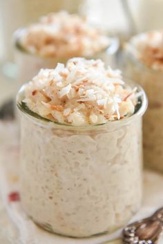 three small glass jars filled with food on top of a white table cloth next to spoons