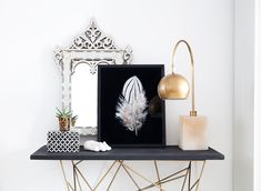 a black shelf with a white feather and a gold lamp on it next to a mirror