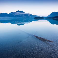 a large body of water with mountains in the background at dusk or dawn, surrounded by low lying rocks