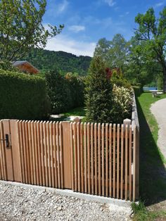 a wooden fence in the middle of a gravel road with trees and bushes behind it