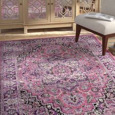 a pink area rug with an ornate design on the bottom and side, in front of a white chair