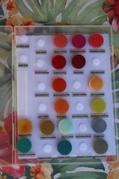 an assortment of different colors of paint in a tray on a flowered tablecloth