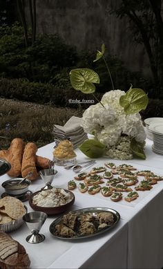 a table topped with plates and bowls filled with food next to flowers on top of a white table cloth