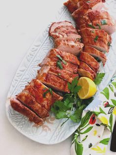 sliced meat on a plate with parsley and lemon wedges