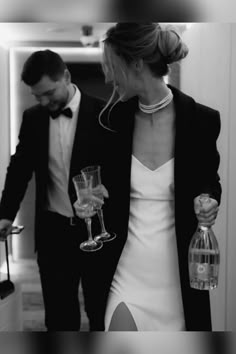 a man and woman are walking down the hallway with wine glasses in their hand,