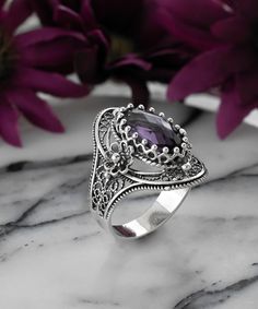 "Beautifully designed and crafted, this February birthstone Amethyst oval ring is a statement piece. The ring face is made from sterling silver and features a high polished finish that reflects light beautifully. It has beautifully two daisy figures on both sides. It comes in sizes 5 to 12.5 with half sizes and has double side faceted, checkerboard oval cut amethyst gemstone on its top add more beauty to the piece. The high-quality sterling silver used in this design ensures durability, while ke Silver Oval Amethyst Ring With Gemstone Accents, Oval Silver Amethyst Ring With Gemstone Accents, Oval Amethyst Ring With Gemstone Accents In Sterling Silver, Handmade Elegant Oval Amethyst Ring, Elegant Handmade Oval Amethyst Ring, Unique Silver Oval Amethyst Ring, Silver Oval Crystal Ring With Gemstone Accents, Fine Jewelry Amethyst Ring With Oval Stone Setting, Fine Jewelry Oval Amethyst Ring