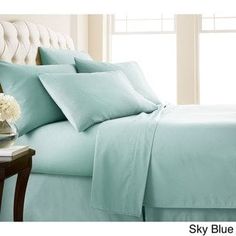 a bed with blue sheets and pillows on top of it next to a vase filled with flowers