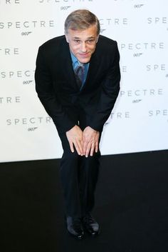 a man in a suit and tie posing for the camera with his hands on his knees