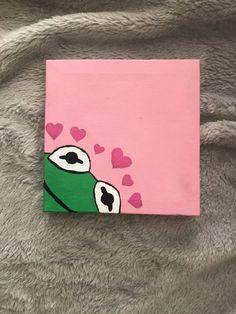 a painting of a green frog with hearts on it's chest and eyes painted on pink paper