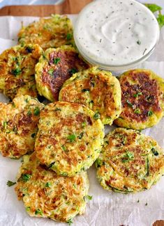 several crab cakes on a piece of parchment paper with a small bowl of ranch dressing in the background