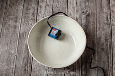 a white bowl with an orange and blue object in it on a wooden floor next to a black cord