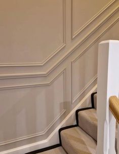 a staircase with beige carpeting and white railings next to a wooden handrail