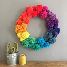 a rainbow colored wreath on the wall next to a cactus