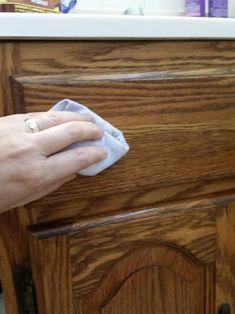 a person wiping up some wood with a cloth on top of the cupboards in their kitchen