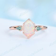 an opal and green diamond ring on a white surface