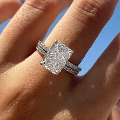 a woman's hand with a diamond ring on top of her finger and the sky in the background