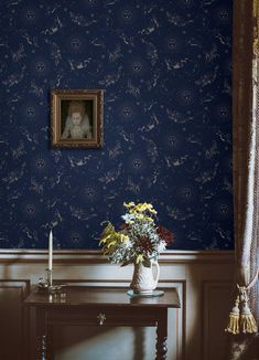 a vase with flowers sitting on a table in front of a wallpapered room