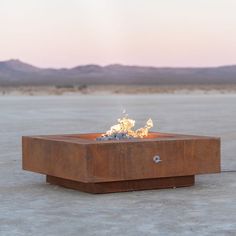 a square fire pit sitting in the middle of a desert field with mountains in the background