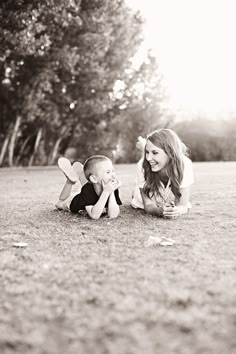 a woman laying on the ground next to a baby in black and white with trees behind her