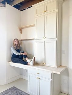 a woman sitting on top of a kitchen counter next to white cupboards and cabinets