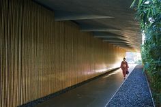 a woman walking down a sidewalk next to a tall bamboo wall on the side of a building