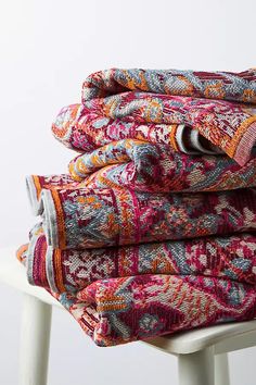 stack of colorful blankets sitting on top of a white chair