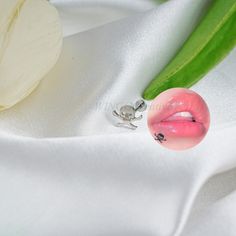 a pink lip ring sitting on top of a white cloth next to a green plant