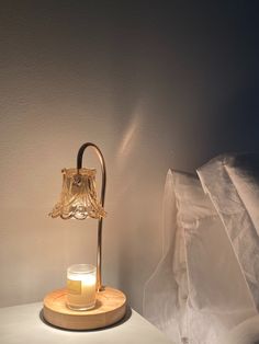 a glass candle on a wooden stand next to a bed