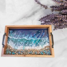 a wooden tray with an ocean scene painted on it and lavender flowers in the background