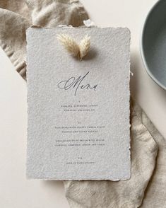 a menu card with a feather on it next to a bowl and napkins that have been folded into them