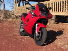 a red motorcycle parked in front of a wooden structure with stairs on the other side