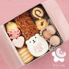 an open box filled with lots of different types of cookies and pastries on top of a pink table