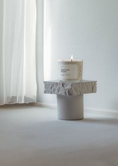 a white candle sitting on top of a stone block next to a window sill