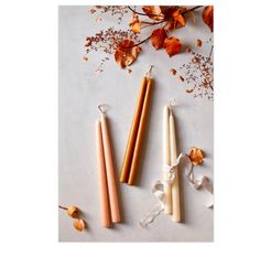 three candles sitting next to each other on top of a white surface with dried flowers