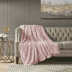 a couch with a pink blanket on top of it in front of a painting and table