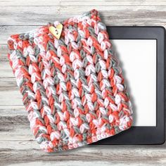 an orange and gray knitted hat sitting on top of a tablet computer next to a wooden table