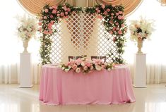 a table with pink cloth and flowers on it in front of a curtained window